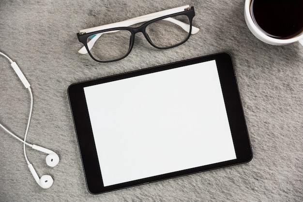 Auricular blanco; los anteojos; Taza de café y tableta digital de pantalla en blanco en el escritorio gris