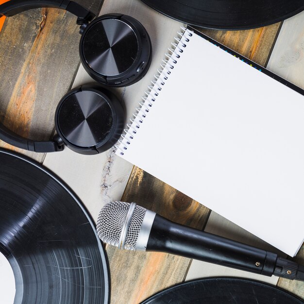 Auricular; micrófono; Disco de vinilo y bloc de notas en espiral sobre mesa de madera.