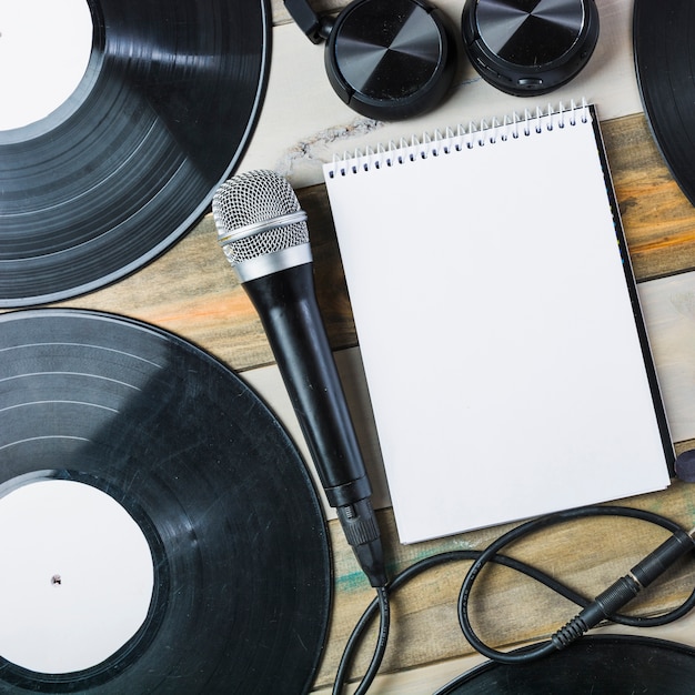 Auricular; micrófono; Disco de vinilo y bloc de notas en espiral sobre mesa de madera.