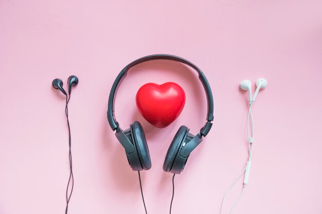 Auriculares alrededor del corazón rojo con dos auriculares contra el fondo rosado