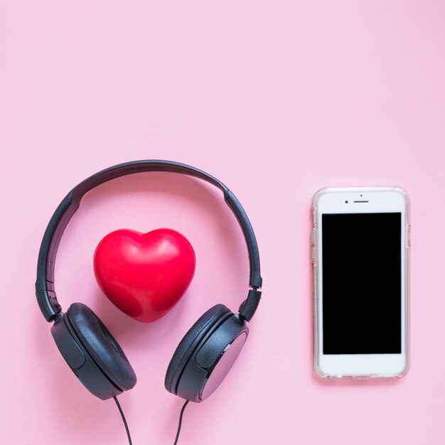 Auriculares alrededor de la forma de corazón rojo y teléfono inteligente contra el fondo rosa