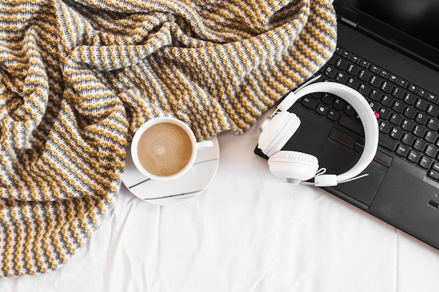 Auriculares y computadora portátil cerca de la manta y café