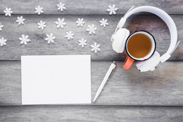 Auriculares y té cerca de los copos de nieve y la hoja de papel