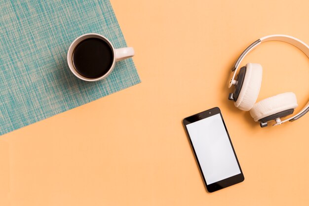 Auriculares con teléfono inteligente y taza sobre fondo naranja