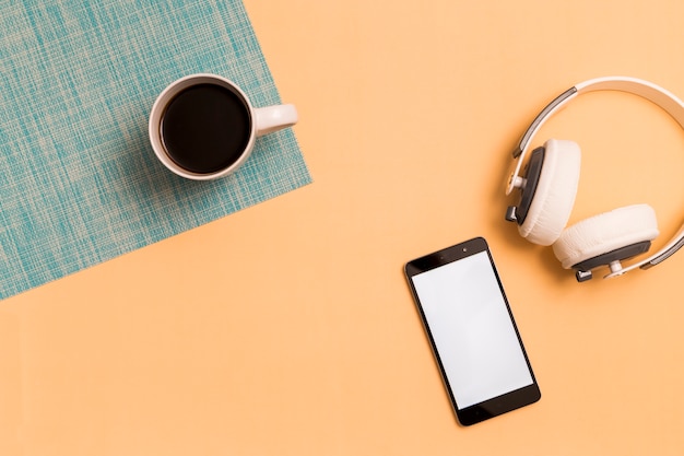 Auriculares con teléfono inteligente y taza sobre fondo naranja