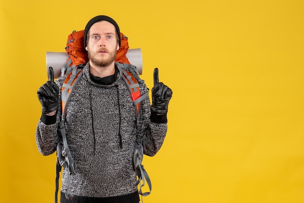 Autoestopista masculino con guantes de cuero y mochila apuntando con los dedos hacia arriba