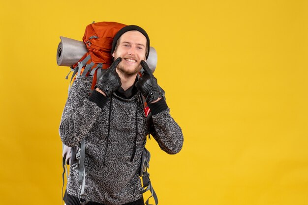 Autoestopista masculino con guantes de cuero y mochila apuntando a su sonrisa