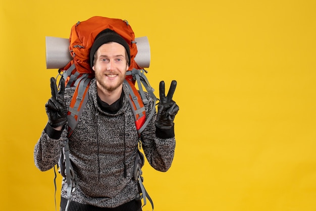 Autoestopista masculino con guantes de cuero y mochila gesticulando signo v