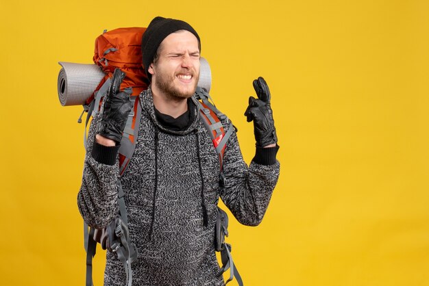 Autoestopista masculino con guantes de cuero y mochila haciendo signo de deseo