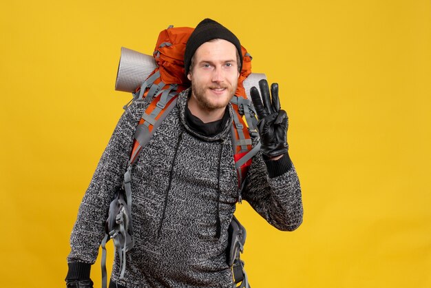 Autoestopista masculino con guantes de cuero y mochila mostrando tres dedos