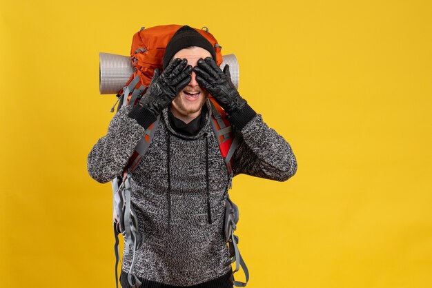 Autoestopista masculino con guantes de cuero y mochila que cubre los ojos con las manos