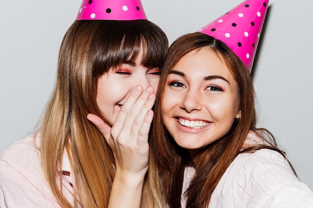 Foto gratuita autorretrato de dos mujeres con sombreros de cumpleaños de papel rosa. amigos vistiendo pijama rosa. estado de ánimo juguetón.