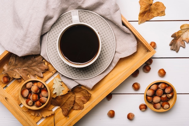 Avellanas y hojas cerca de la bandeja con café