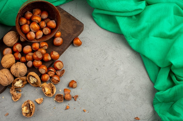 Avellanas y nueces peladas y enteras dentro de una olla marrón sobre un pañuelo verde y luz