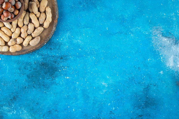 Avellanas en un recipiente a bordo con cacahuetes, sobre la mesa azul.