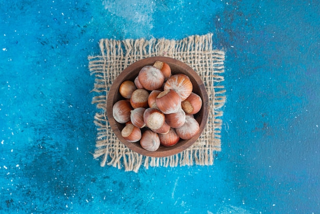 Foto gratuita avellanas en un recipiente de textura, sobre la mesa azul.