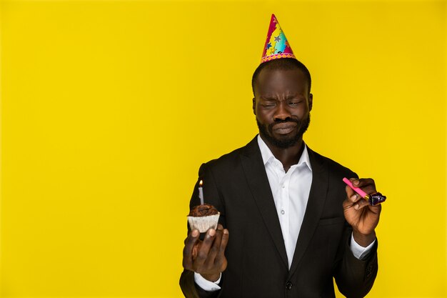 Avergonzado lindo negro sosteniendo un pastel de cumpleaños y un silbato