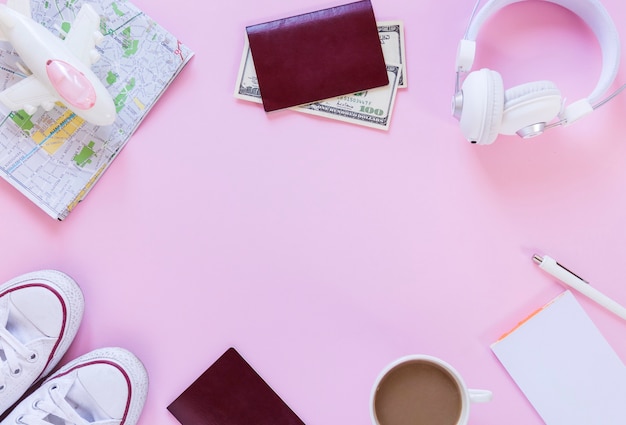 Avión; mapa; pasaporte; billetes de banco calzado; auricular; té; papel y pluma sobre fondo rosa