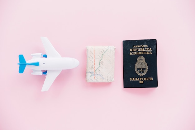 Foto gratuita avion miniatura blanco; mapa y pasaporte sobre fondo rosa