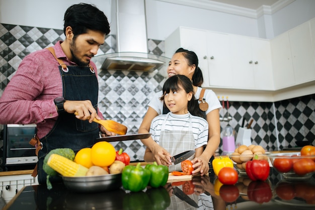 Ayuda feliz de la familia que cocina la comida junta en cocina en casa.