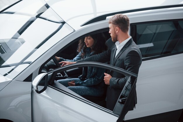 Ayudando a la chica a decidir. Clienta y empresario barbudo con estilo moderno en el salón del automóvil