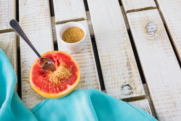 Azúcar marrón y cuchara en pomelo a la mitad con servilleta sobre fondo de madera