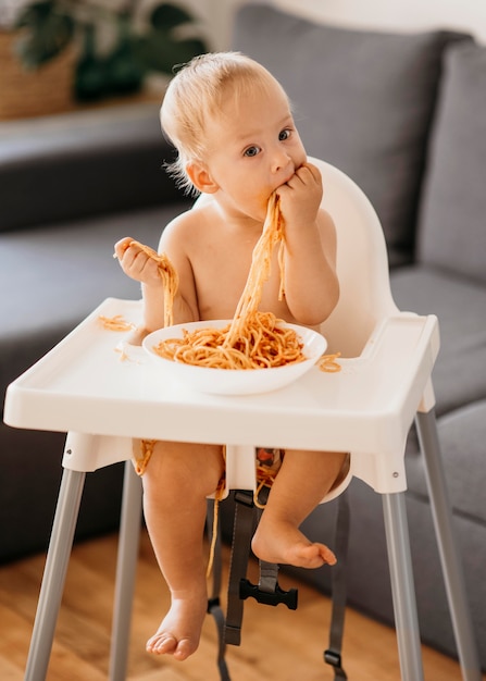 Foto gratuita baby boy jugando con pasta en su trona