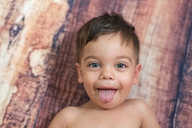 Baby Boy con ojos azules sobre fondo de madera con lengua colgando