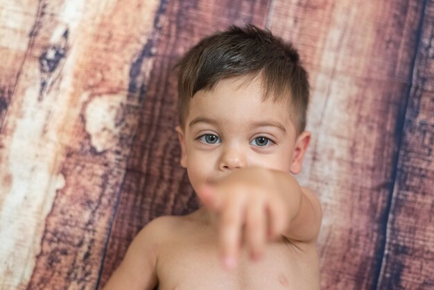 Baby Boy con ojos azules tumbado en la pared de madera