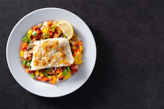 Bacalao a la plancha con verduras en plato sobre fondo de piedra negra