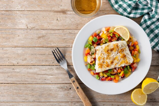 Bacalao a la plancha con verduras en plato sobre mesa de madera