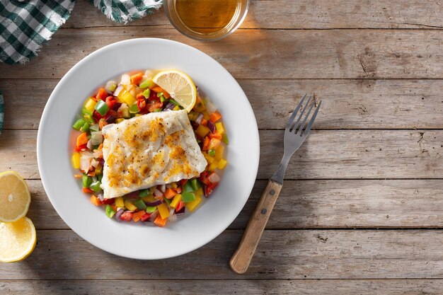 Bacalao a la plancha con verduras en plato sobre mesa de madera