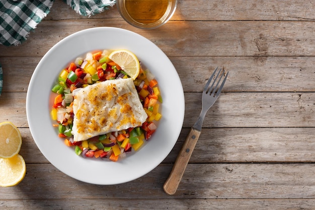 Bacalao a la plancha con verduras en plato sobre mesa de madera