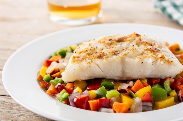 Bacalao a la plancha con verduras en plato sobre mesa de madera