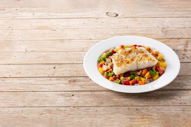 Bacalao a la plancha con verduras en plato sobre mesa de madera