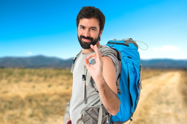 Backpacker haciendo Ok firmar sobre fondo blanco