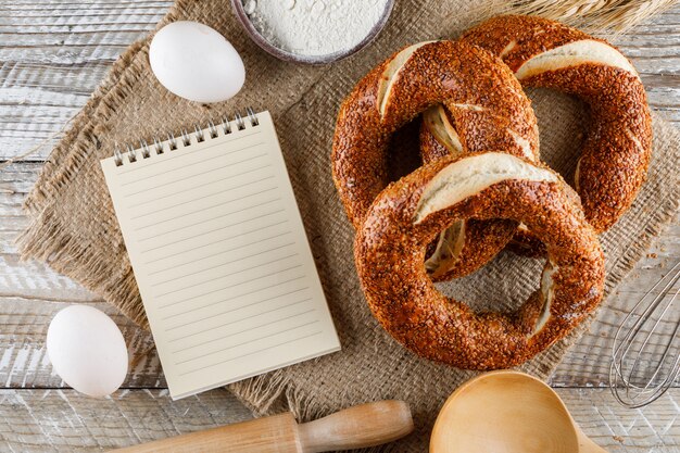 Bagel turco con bloc de notas, huevos, rodillo vista superior sobre un saco de tela y superficie de madera