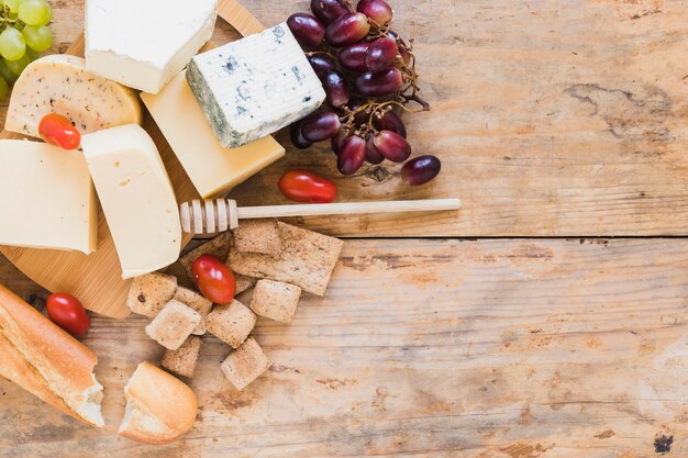 Baguette, bloques de queso con gotero de miel, tomates y uvas en el escritorio de madera