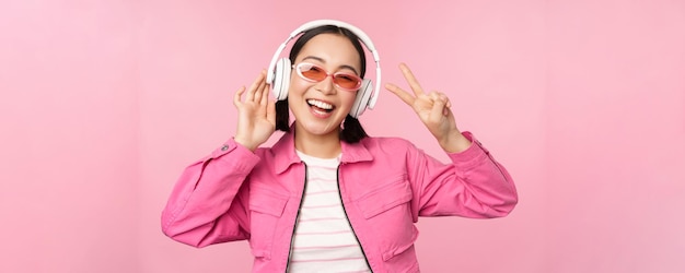 Bailando con estilo chica asiática escuchando música en auriculares posando sobre fondo rosa