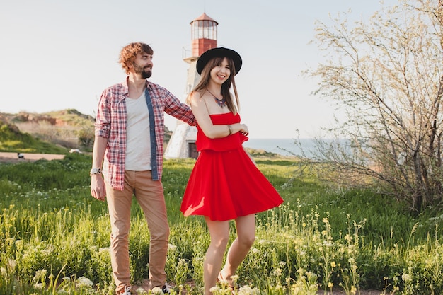 Bailando joven pareja elegante enamorada en el campo, estilo bohemio indie hipster, vacaciones de fin de semana, traje de verano, vestido rojo, hierba verde, tomados de la mano