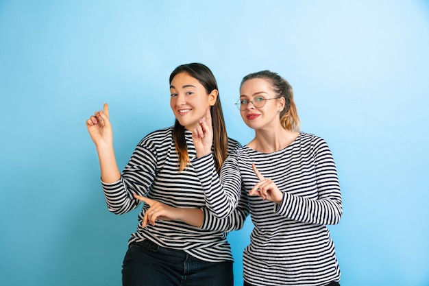 Bailando juntos. Mujeres emocionales jóvenes aisladas en la pared azul degradado. Concepto de emociones humanas, expresión facial, amistad, anuncio. Hermosas modelos femeninas caucásicas en ropa casual.