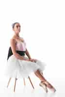 Foto gratuita bailarín de ballet confiado que se sienta en silla con la pierna cruzada contra el contexto blanco