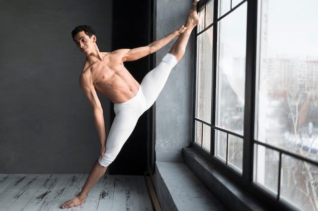 Bailarín de ballet masculino que se extiende junto a la ventana