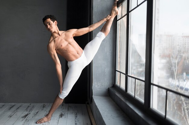 Bailarín de ballet masculino que se extiende junto a la ventana