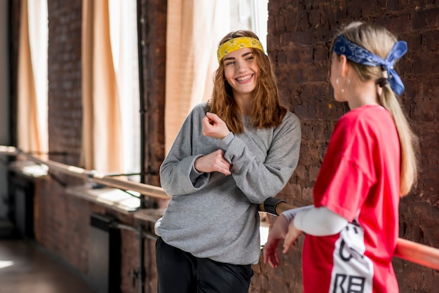 Foto gratuita bailarín de sexo femenino joven sonriente que se coloca cerca de la barra en el estudio de la danza