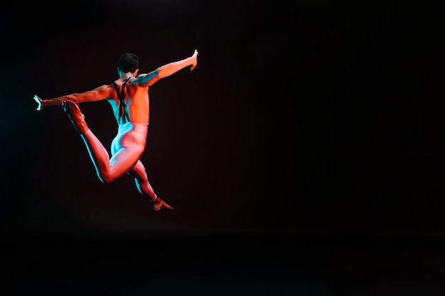 Bailarina de ballet irreconocible saltando con los brazos extendidos y haciendo divisiones