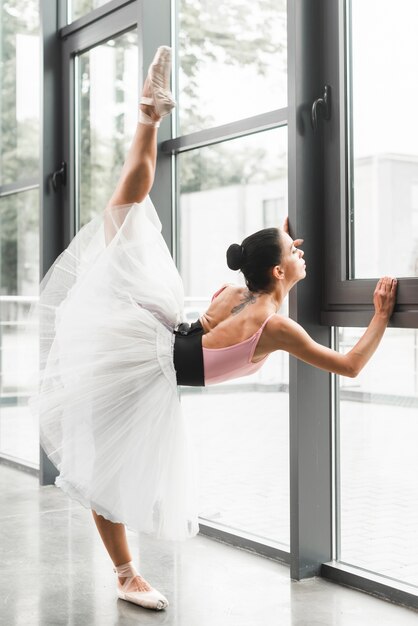 Bailarina femenina estirando su pierna cerca de la ventana