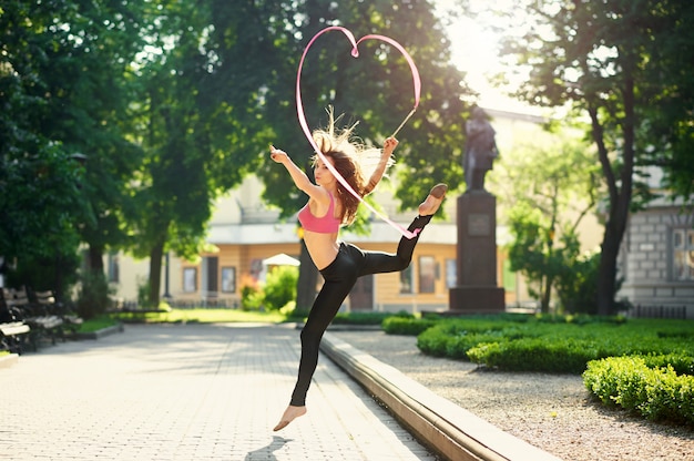 Bailarina haciendo piruetas con una cinta en el parque de la ciudad.