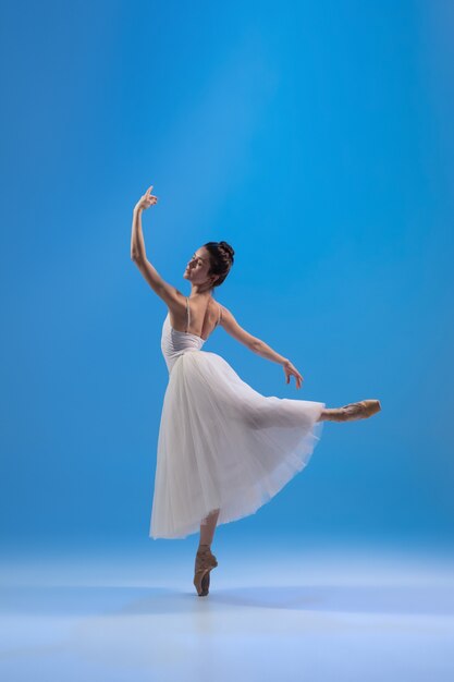 Bailarina joven y elegante en vestido blanco aislado en la pared azul