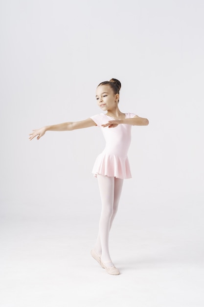 Bailarina de niña delicada de pie en pose de ballet en blanco. Tipos de concepto de desarrollo de la personalidad.